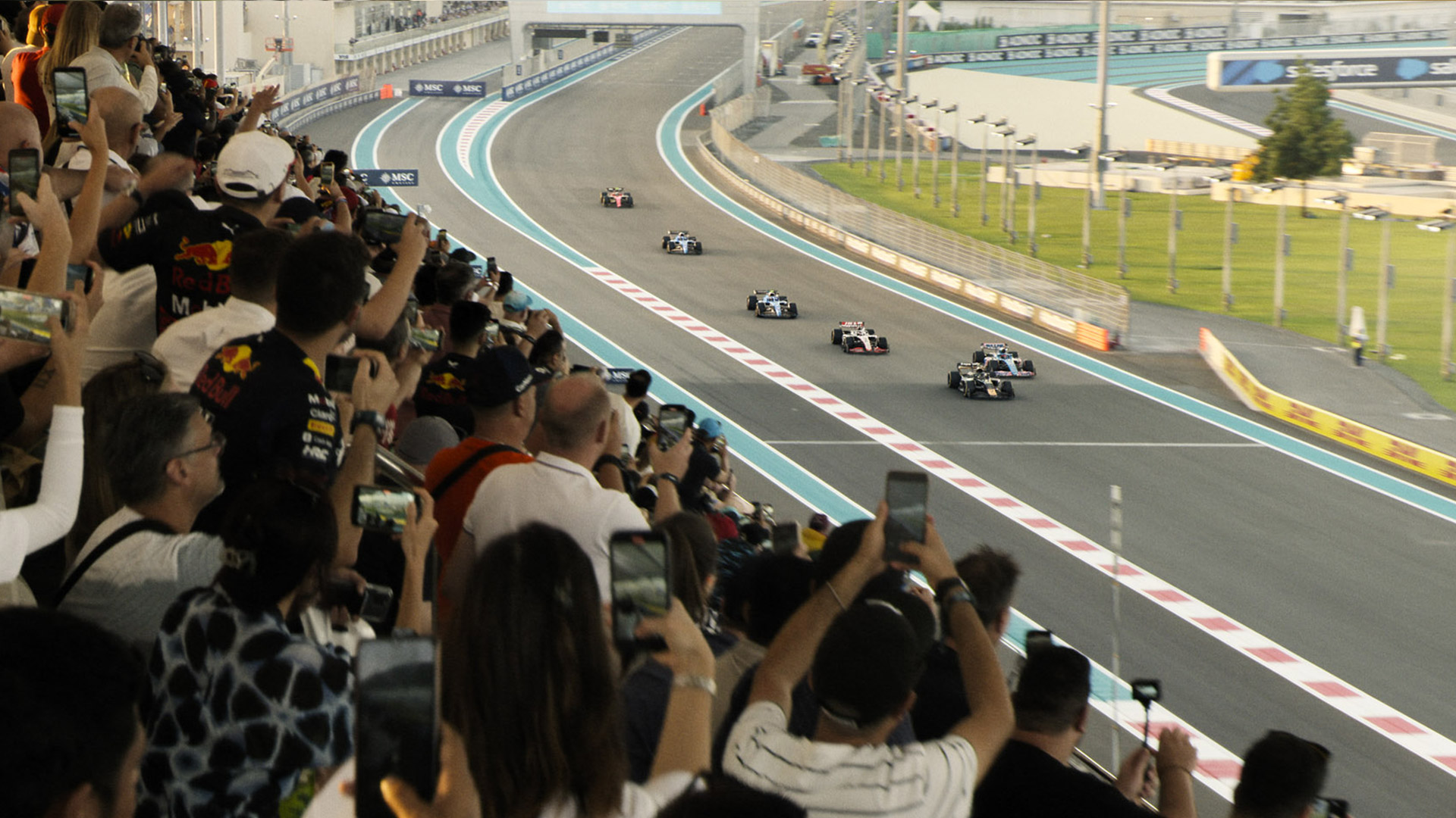 A crowd holds up their phones to capture passing F1 cars