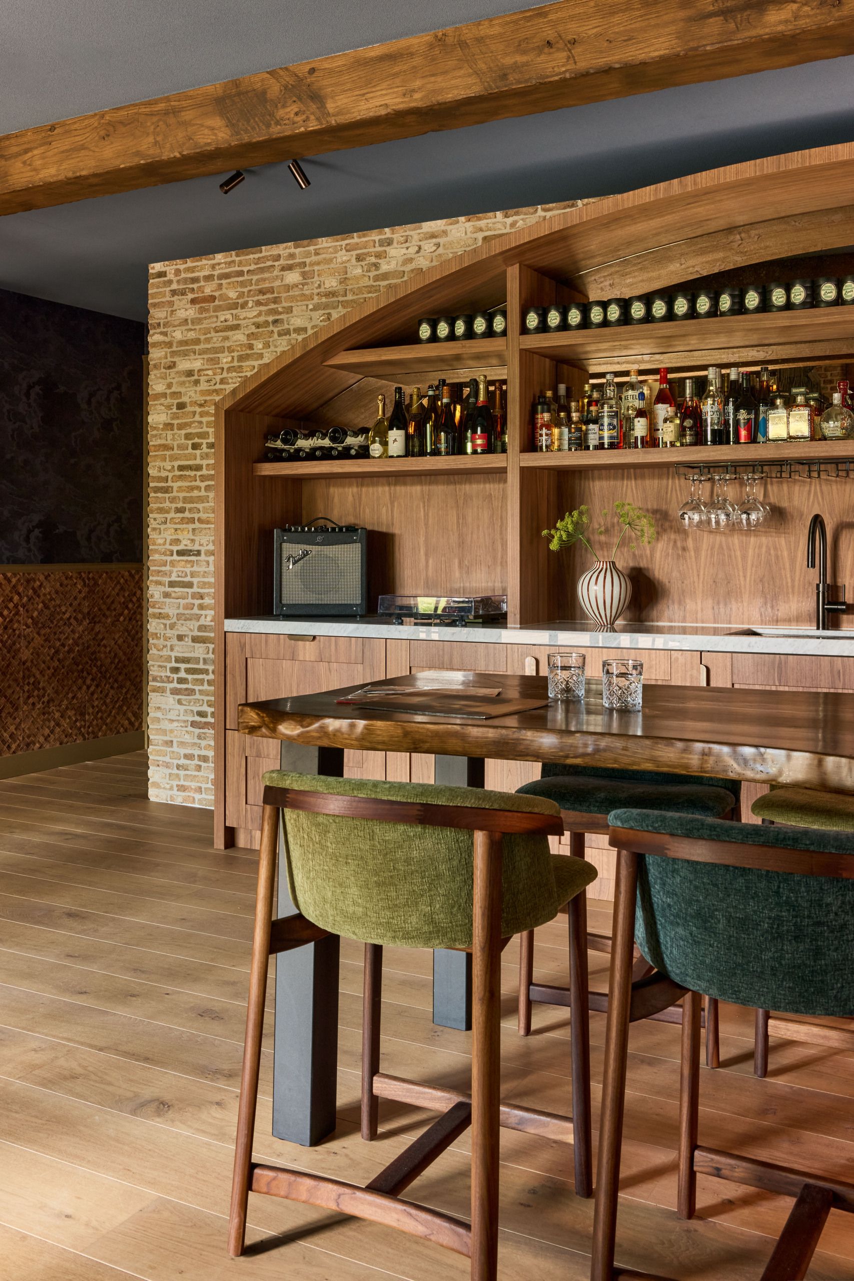A cozy home bar with wooden details and a bar table that has green and blue seat around it.