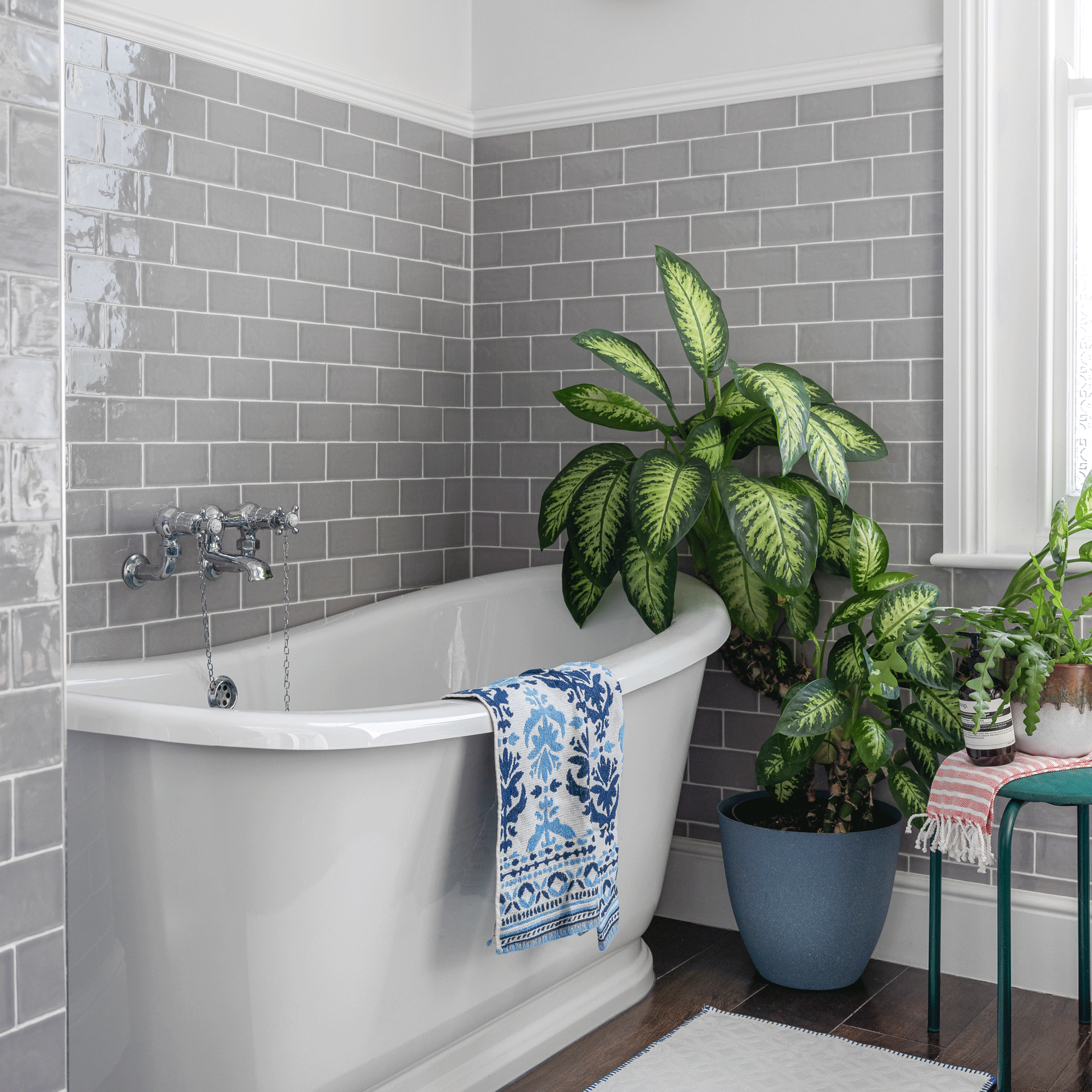 a grey tiled bathroom with white walls and a traditional freestanding bath tub