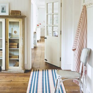 A hallway space with a striped runner rug , a chair and wall hooks
