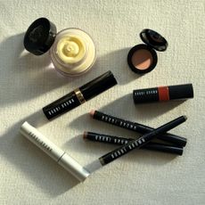 A bird's eye view of a flatlay of a selection of the best Bobbi Brown products featured in this guide, laying on a cream linen background