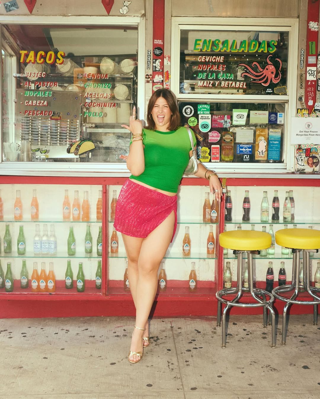 Fashion person Reaann Langas is wearing sequin skirt, green top and matching bag and shoe combination in gold. She is stood in front a taco stand swearing at the camera in a recent image from her Instagram.