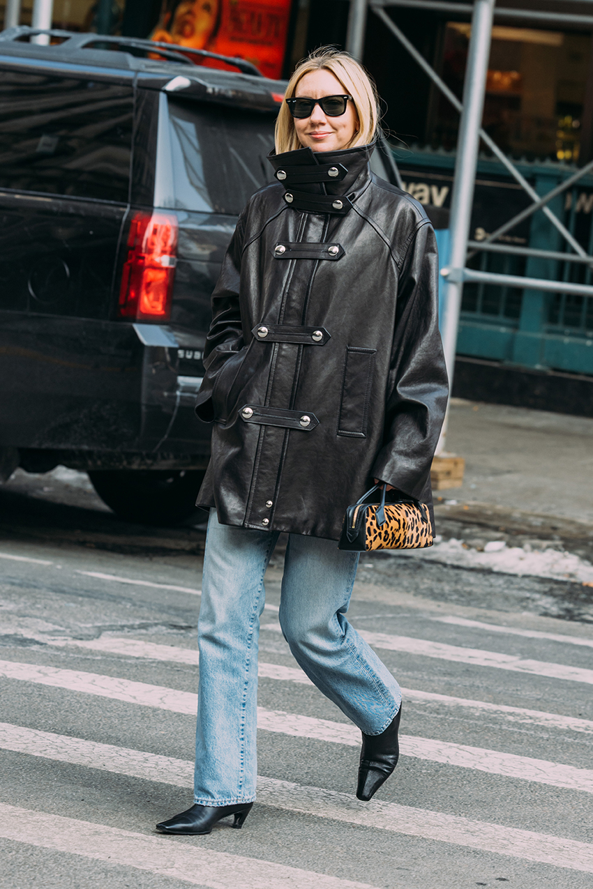 A woman wearing a black leather jacket, blue jeans, and black pointed toe boots