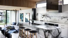 A marbled kitchen island with a backsplash of the same design. Bar stools sit by the island of an open plant space. 