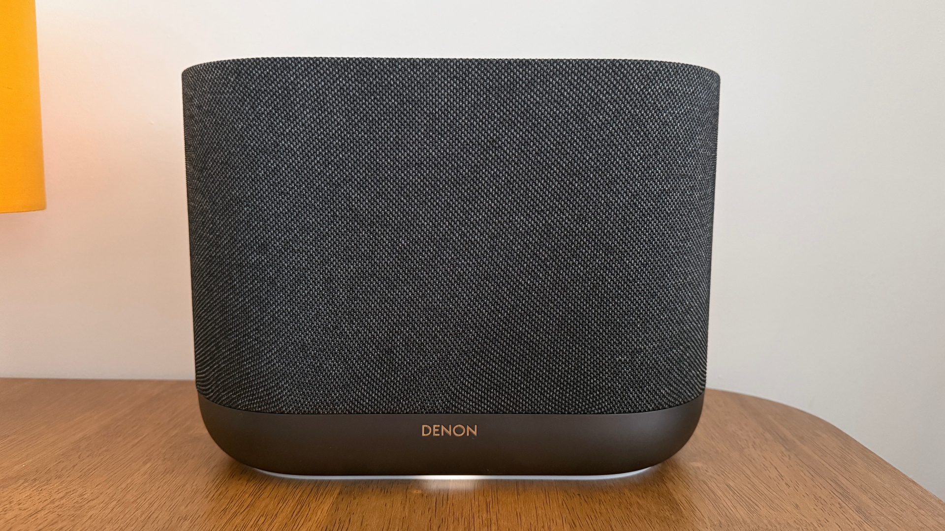 A front-on view of a grey Denon Home 400 wireless speaker on a wooden table.