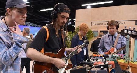 A guitarist wears headphones as he tries out a semi-hollow at NAMM