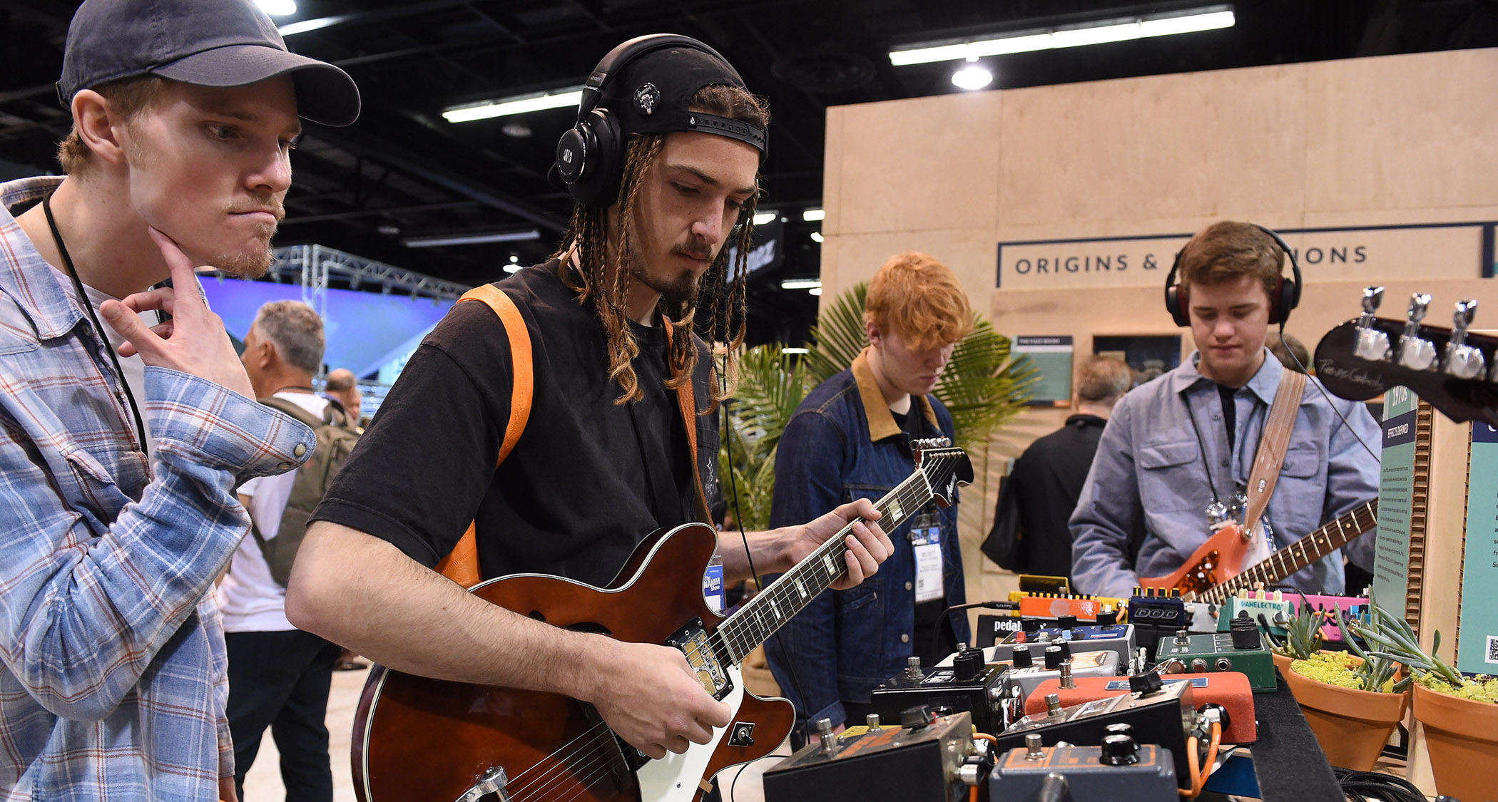A guitarist wears headphones as he tries out a semi-hollow at NAMM