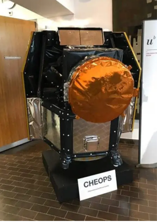 A replica of CHEOPS with a large orange cover over the telescope and a label beneath it reading "CHEOPS".