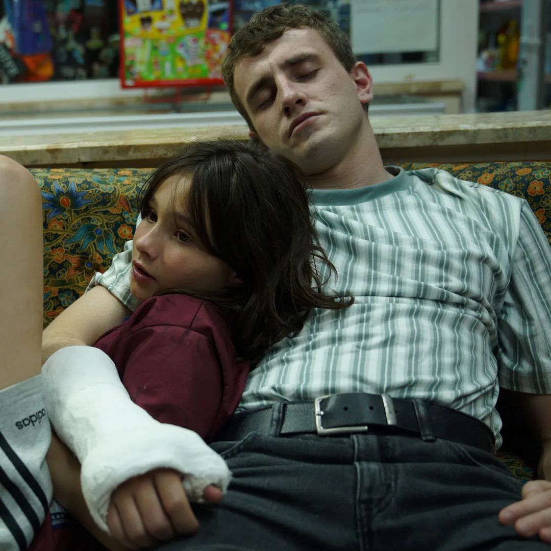 a little girl and her dad laying on a couch in a still from the movie aftersun