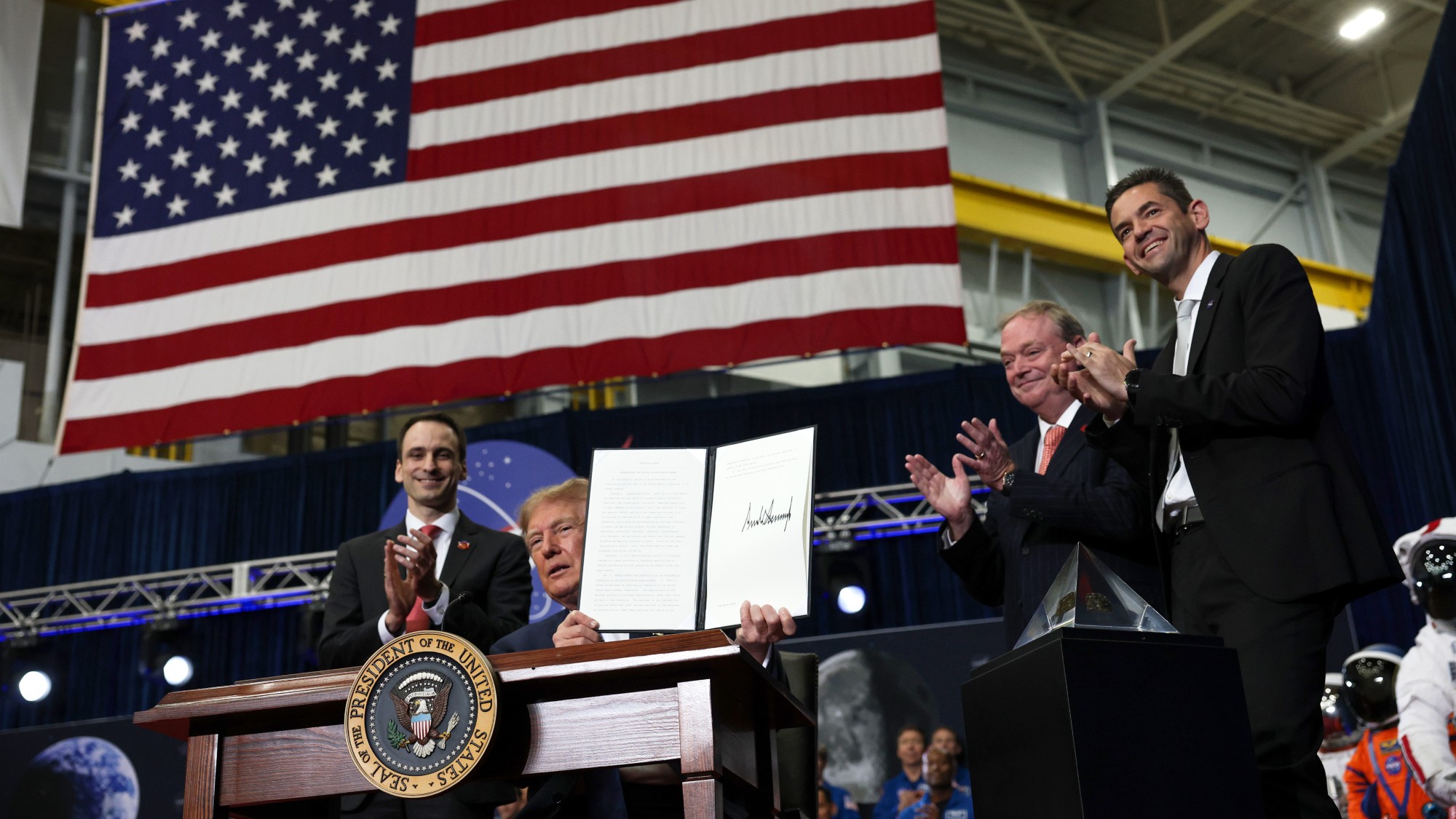 a man in a blue suit holds up a signed document under an american flag