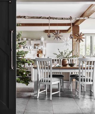 White country kitchen-diner decorated for Christmas with paper decorations and natural foliage