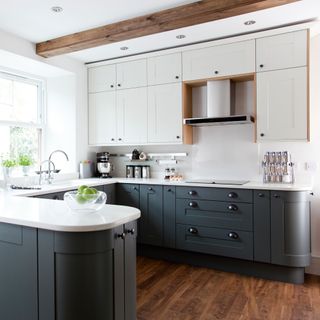 Kitchen with white and green-grey cabinetry, wooden floor and wooden beam