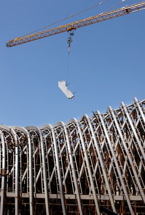 Close up view of the Phoenix TV building during the construction phase under a clear blue sky. There is a structural element hanging from a yellow crane above the building