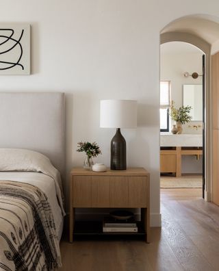 White bedroom with private bathroom view, wooden floor, wooden bedside, stone bed, neutral bedding