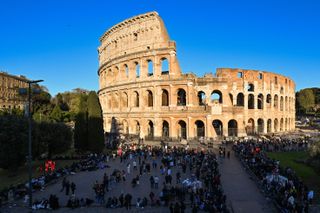 The Colosseum surrounded by visitors on a clear blue sky day