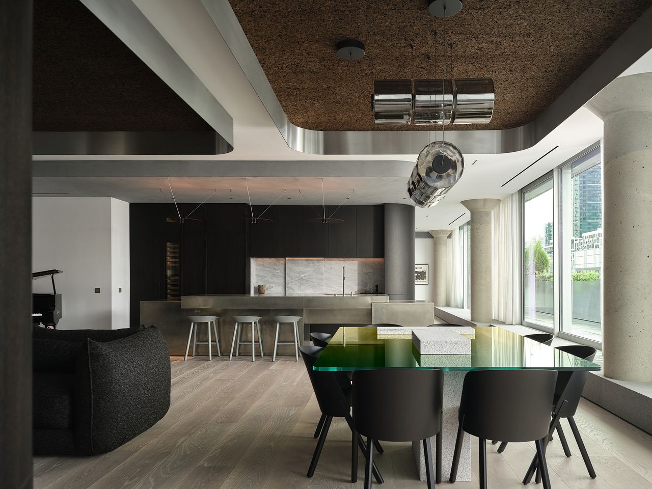 modern open plan dining room and kitchen with stainless steel cabinetry, concrete details, green glass dining table, cork ceiling, and floorboards