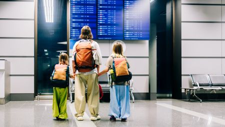 A mother and her two kids check the flight schedule at the airport.