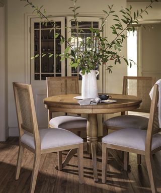 A light wood kitchen table in the centre of a white kitchen with four chairs