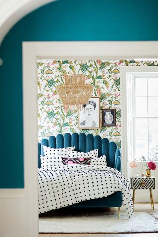 a blue velvet bed in a bedroom with wallpaper and clashing prints