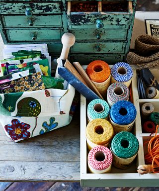 An aerial view of colorful balls of twine and packets of seeds on a wooden work shelf with minty blue mini drawers.