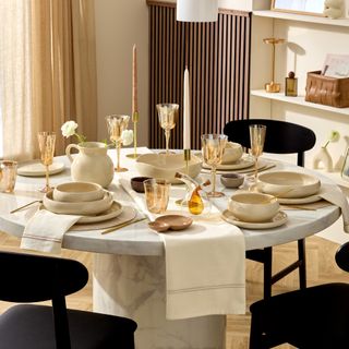 A round marble dining table set with glazed cream tableware and amber-coloured glassware from the Minimaluxe trend