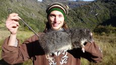 Man stands holding a massive rat.