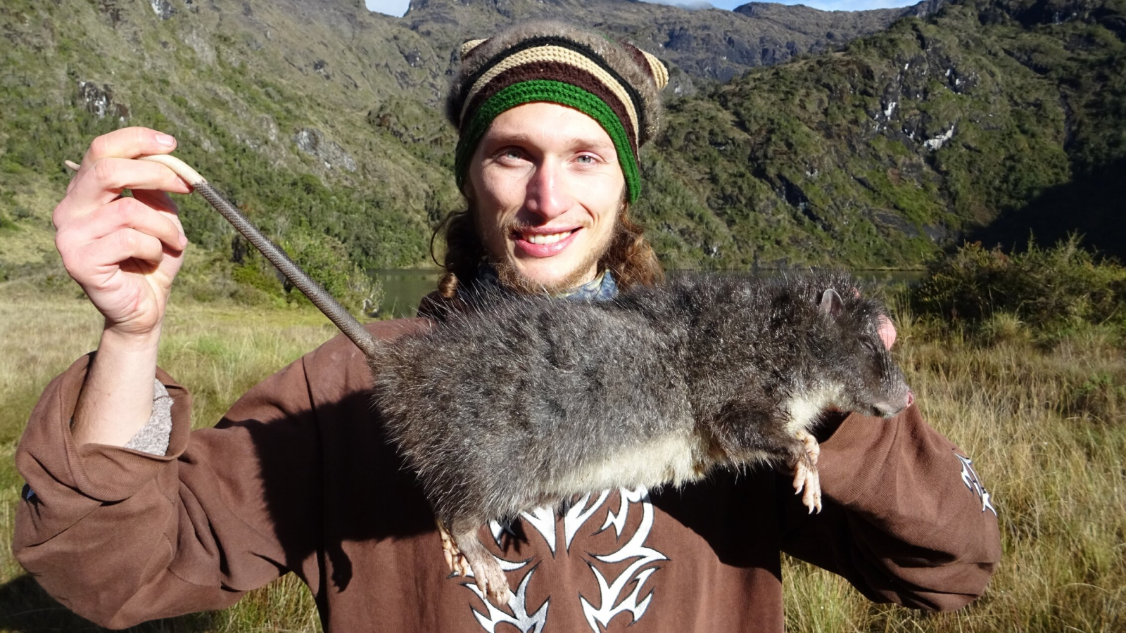 Man stands holding a massive rat.
