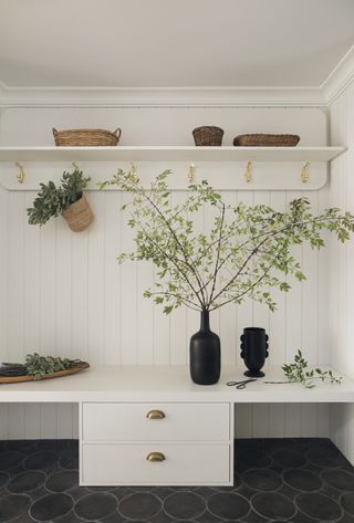 Two black vases sit by an entryway with green foliage scattered around the space. Baskets are placed on open shelving