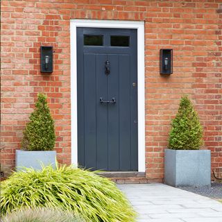 Grey front door flanked by topiary and wall lights