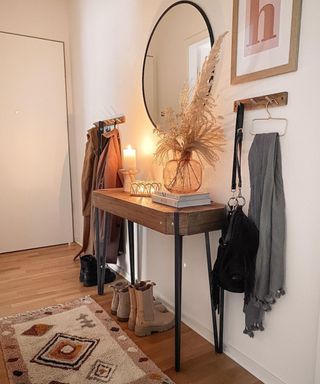 A small hallway decorated in a bohemian style with black framed mirror, wooden console table, wooden coat hooks and boho style runner carpet