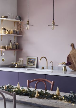 Christmas kitchen with foliage and fairy lights, lilac walls and purple units