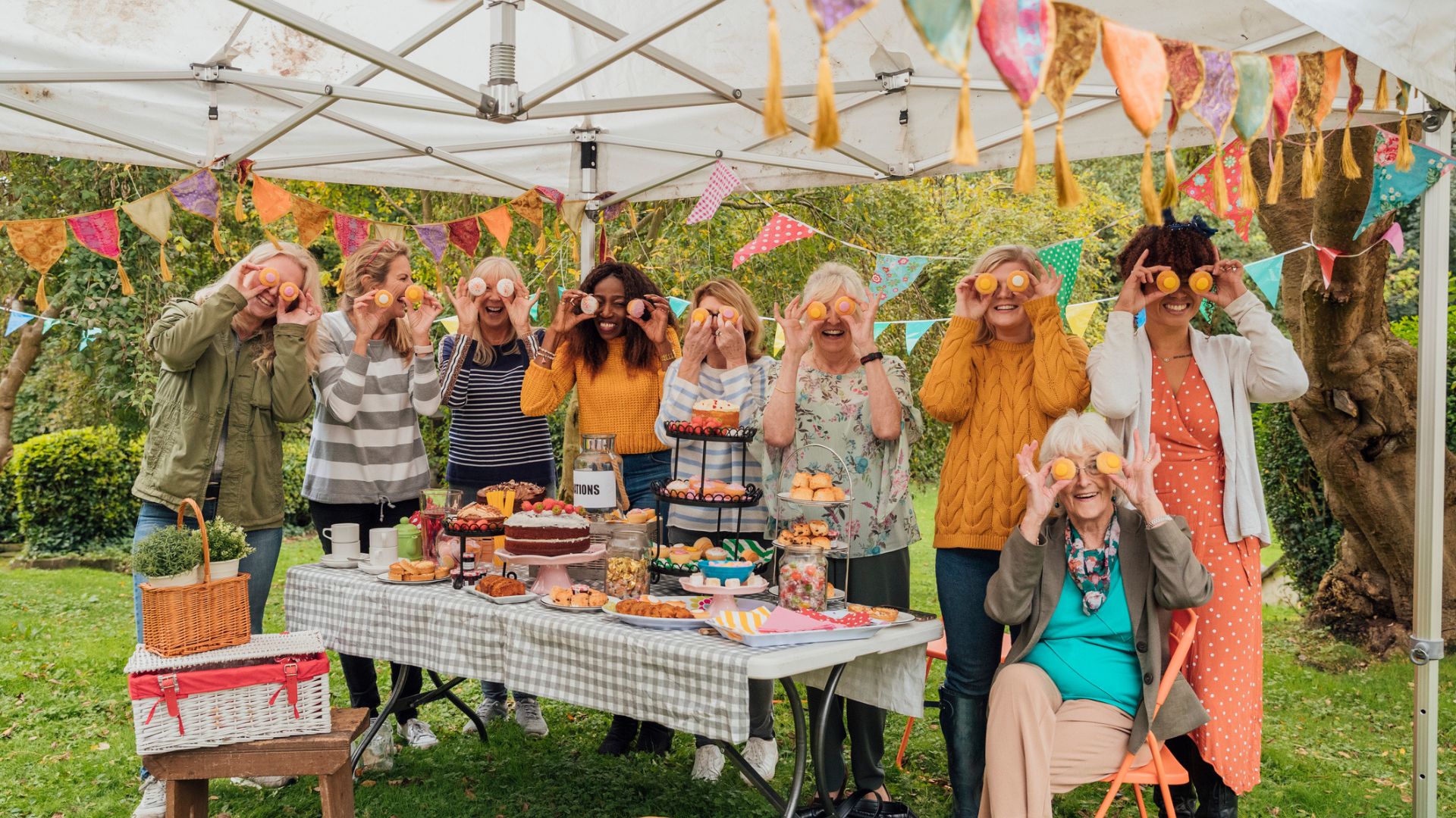 A group of women gather around an array of cakes in a tent