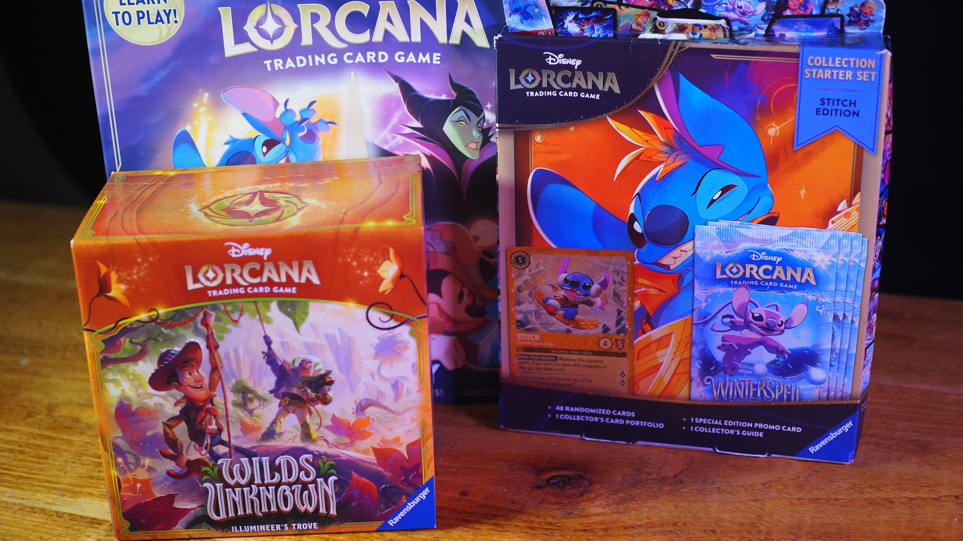 A Disney Lorcana Gateway box, Stitch Collection Starter Set box, and Wilds Unknown Illumineer's Trove on a wooden table