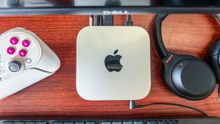The Apple Mac mini M4 on a desk with a controller, headphones and keyboard