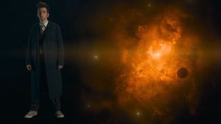 David Tennant standing in front of a green screen of a galaxy