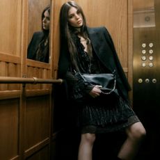 Model in a wooden lift wearnig a black blazer and black dress holding a black bag sold at Zadig & Voltaire