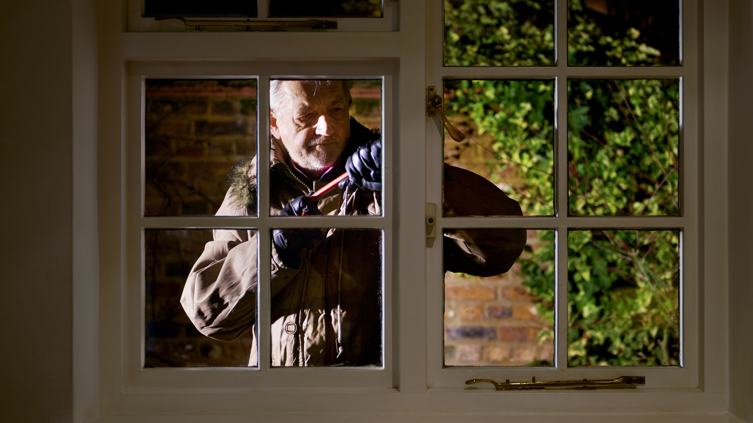 Window seen from the interior of the home with man outside attempting to force it open