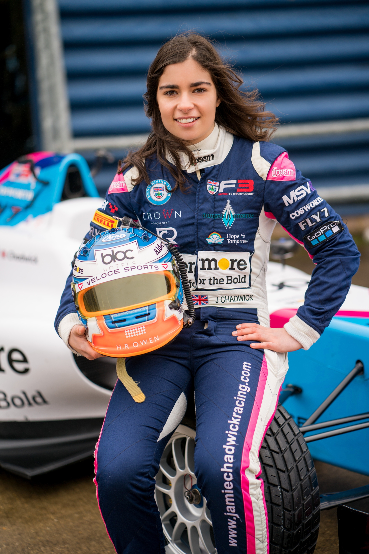 Jamie Chadwick holding her helmet and sat on the nose of a racecar