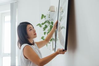 A young women hanging a photo on her wall.