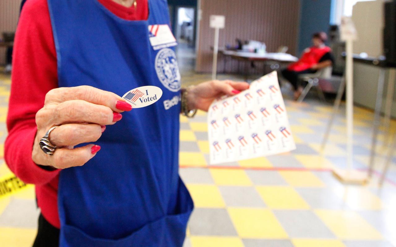 Photo of woman handing out &amp;quot;I voted&amp;quot; sticker