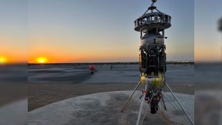 a cylindrical spacecraft stands up right in the desert above illustrations of the moon's surface on the ground