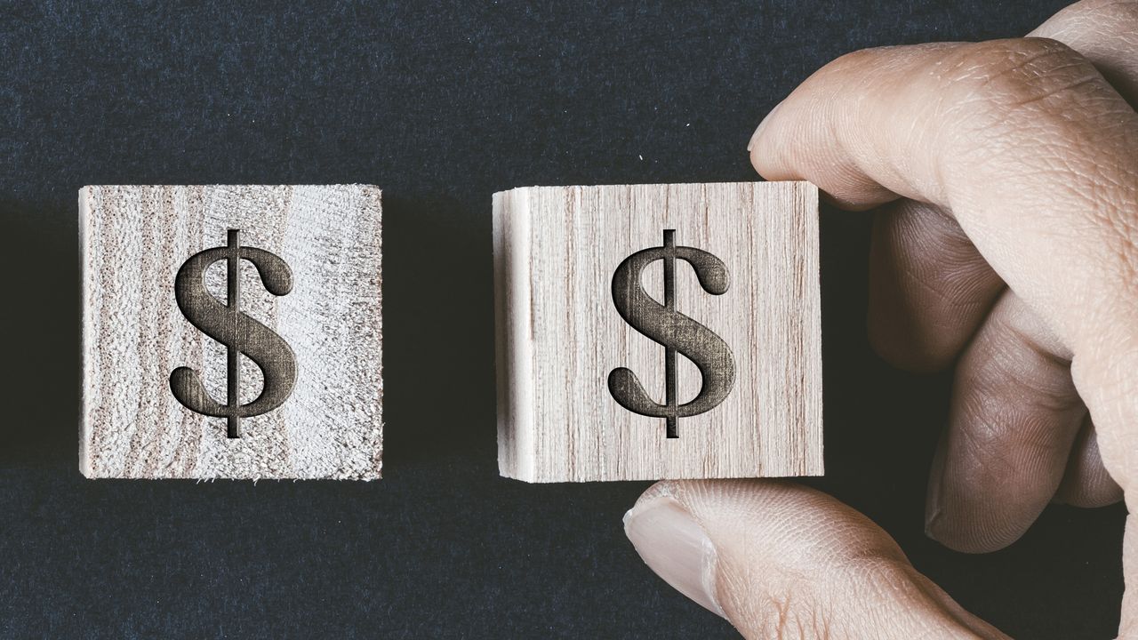 A man&#039;s fingers hold one of two wooden blocks with dollar signs on them.