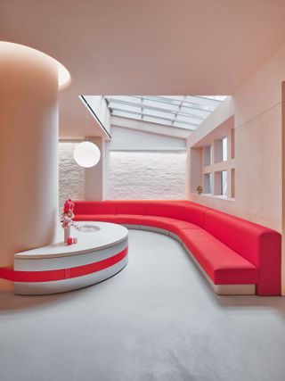 Red seating curved around the wall beneath a skylight in Glossier store New York