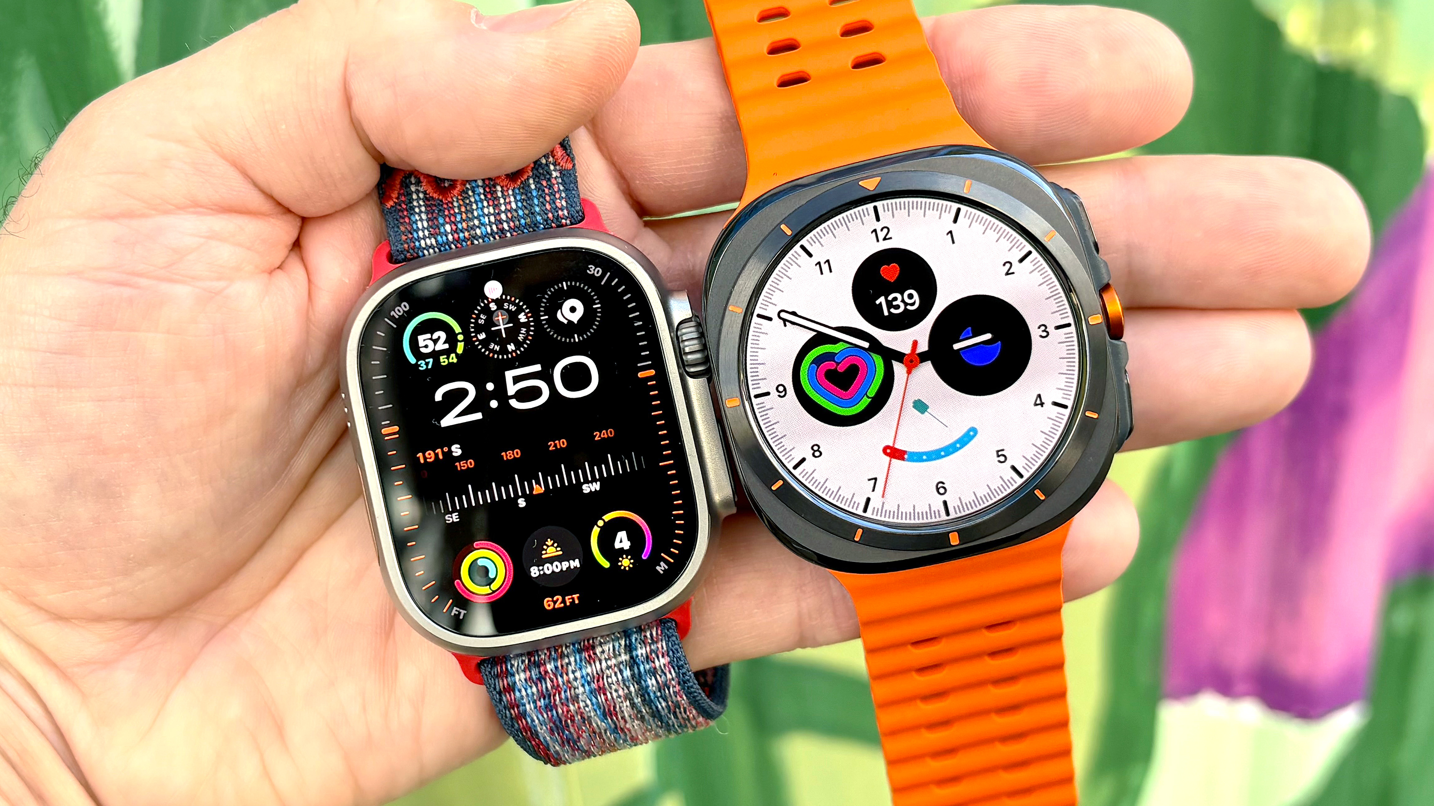 Close-up of the Apple Watch Ultra 3 next to the Samsung Galaxy Watch Ultra in the writer's hand against a colorful background