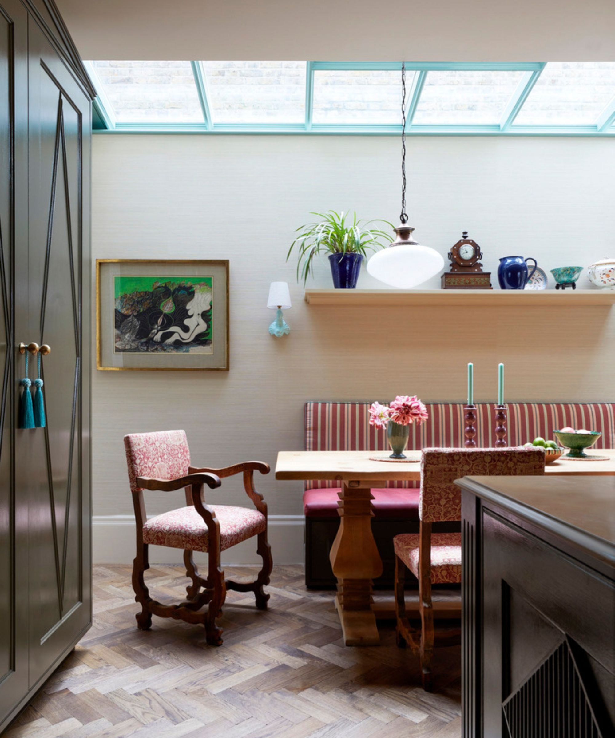 A large kitchen with dark green cabinets, wood herringbone flooring, and a red and white striped dining banquette