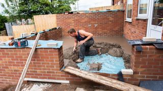 A builder laying concrete screed inside red brick walls 