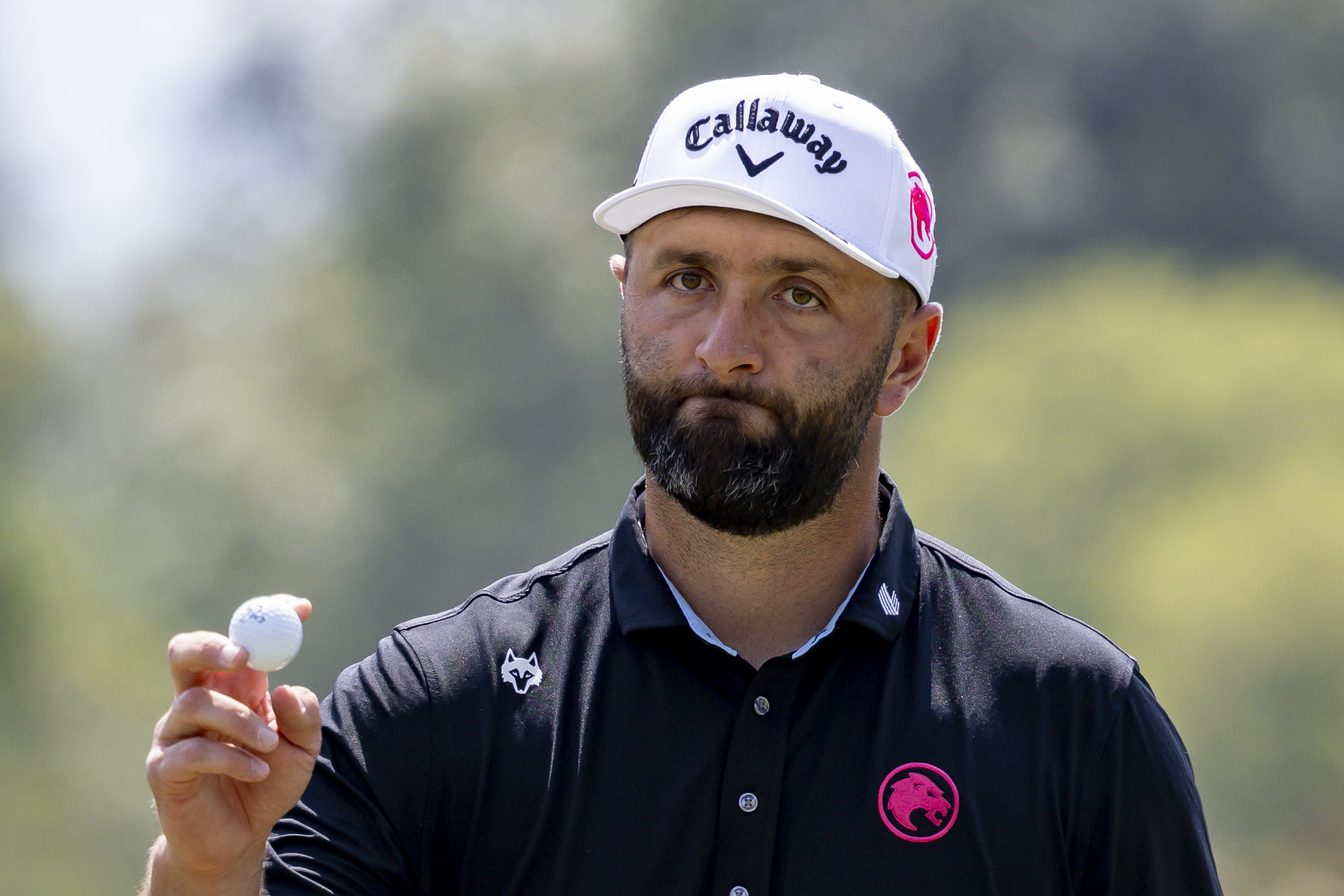 Jon Rahm waves to the crowd holding a golf ball