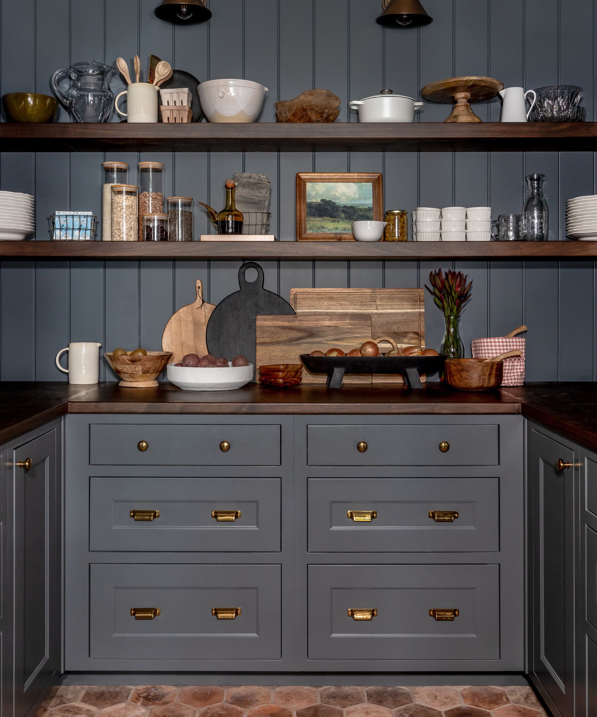navy blue back kitchen pantry with terracotta floor tiles, blue wooden panelled backsplash and open shelves styled with vintage pieces and art