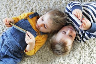 Two children laying on the floor watching mobile phones