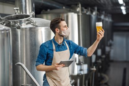 A brewery worker tastes beer and enters notes onto a tablet